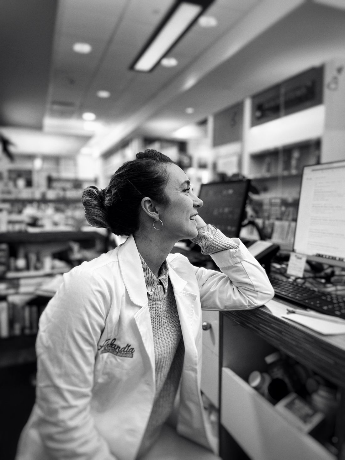 Farmacéutica usando un ordenador en el mostrador de una farmacia para atender a sus clientes